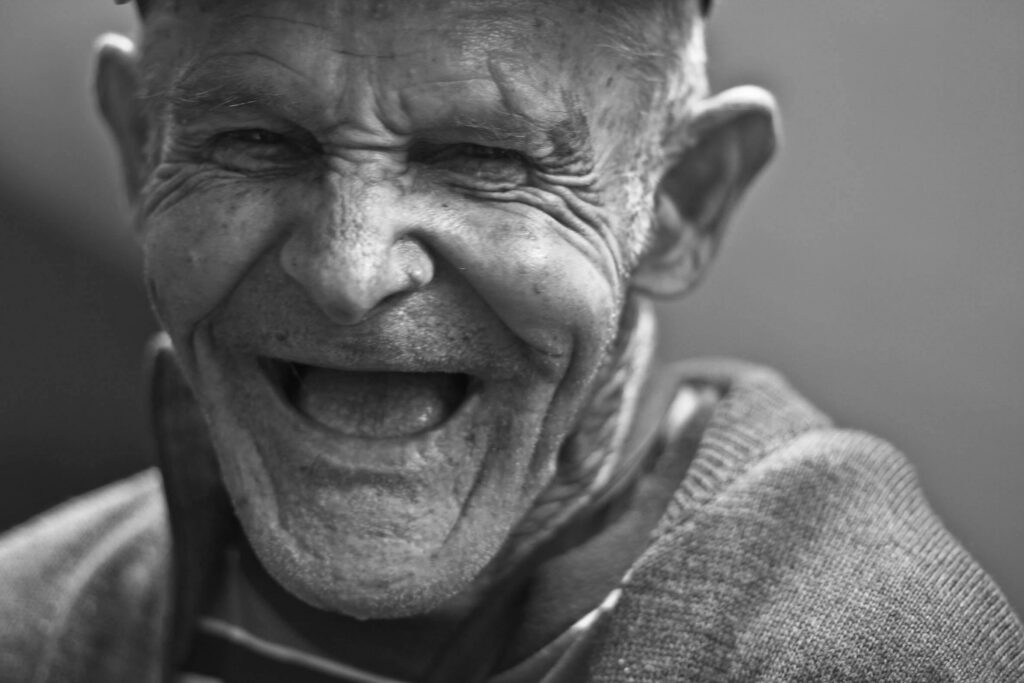 Close-up portrait of an elderly man laughing, capturing a joyful and emotive expression.